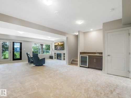 Expansive carpeted room featuring a built-in wet bar with cabinetry, sink, and beverage refrigerator - 3 1641 James Mowatt Trail, Edmonton, AB 