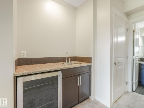 Wet bar featuring a stainless steel beverage refrigerator, compact sink, granite-style countertop, and dark wood-finish cabinetry - 3 1641 James Mowatt Trail, Edmonton, AB 