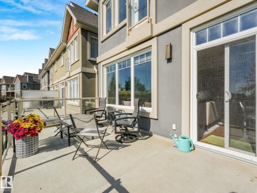 Spacious main level deck featuring a glass railing, exterior sconce lighting, and multiple large windows - 3 1641 James Mowatt Trail, Edmonton, AB 