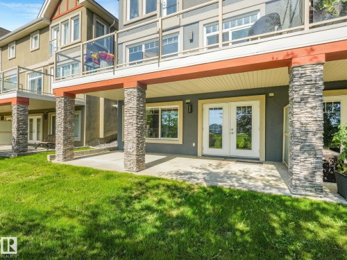 Ground-level patio with double French doors, surrounded by stacked stone columns, and featuring a manicured lawn - 3 1641 James Mowatt Trail, Edmonton, AB 