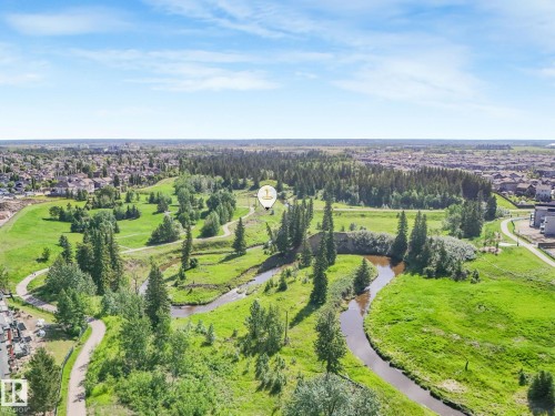 Expansive green space featuring a winding river, numerous mature trees, paved pathways, and a bridge structure - 3 1641 James Mowatt Trail, Edmonton, AB 