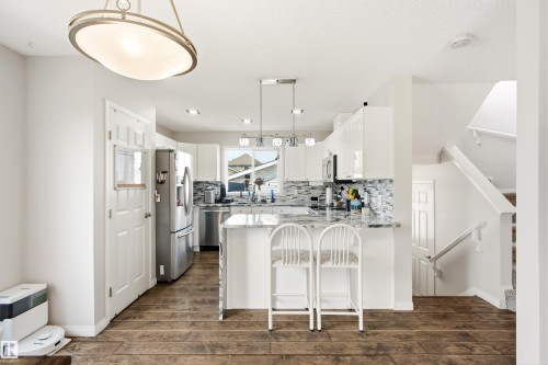 Kitchen featuring white cabinetry, stainless steel appliances, a tile backsplash, and a breakfast bar island with a light-toned countertop - 21384 88 Avenue, Edmonton, AB 