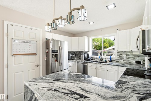Kitchen featuring white cabinetry, striking granite countertops, stainless steel appliances, a glass tile backsplash, and recessed and pendant lighting - 21384 88 Avenue, Edmonton, AB 