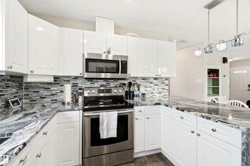 Modern kitchen featuring white cabinetry, a glass tile backsplash, and dark patterned countertops - 21384 88 Avenue, Edmonton, AB 