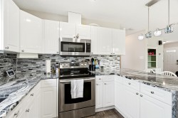 Modern kitchen featuring white cabinetry, a glass tile backsplash, and dark patterned countertops - 