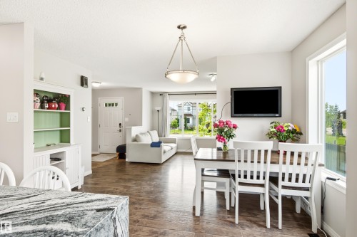 Open-concept main living area featuring wood-finish flooring, a contemporary ceiling fixture, large windows, and a built-in wall television mount - 21384 88 Avenue, Edmonton, AB 