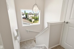 Staircase featuring carpeted treads, white painted handrails, and a modern chandelier - 