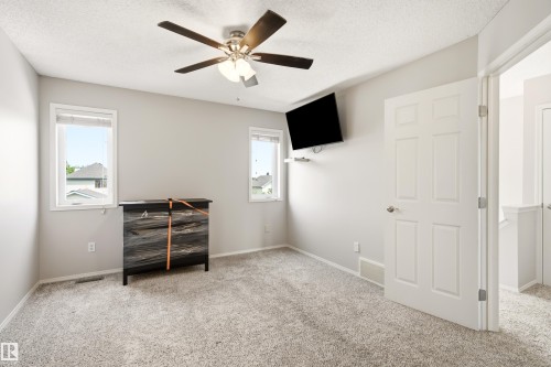 Carpeted room featuring a ceiling fan with integrated lighting, two windows with white trim, and a white six-panel door - 21384 88 Avenue, Edmonton, AB 