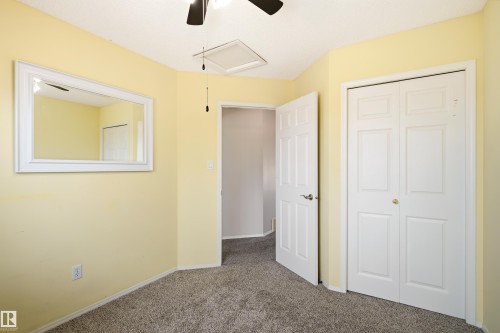 Bedroom featuring light yellow walls, textured carpet flooring, a white bi-fold closet door, a white six-panel door, and a ceiling fan - 21384 88 Avenue, Edmonton, AB 