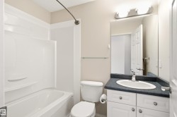 Full bathroom featuring a white tub/shower combination, white toilet, and a vanity with a dark countertop and white cabinetry - 