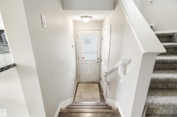 Carpeted staircase with white handrail and trim, leading to a landing with wood-finish flooring and a white exterior door featuring a window with grid pattern - 
