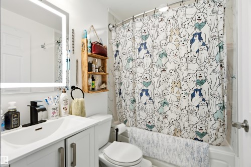 Bathroom featuring a white vanity with integrated sink, black single-handle faucet, illuminated rectangular mirror, and a white toilet - 21384 88 Avenue, Edmonton, AB 