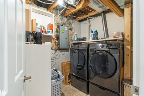 Dedicated laundry area featuring a stacked washer and dryer, adjacent shelving, a utility panel, and exposed ceiling joists - 21384 88 Avenue, Edmonton, AB 