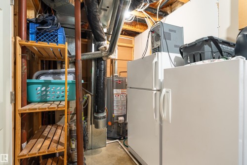 Basement utility area featuring two freestanding refrigerators, exposed ceiling joists, and a hot water heater - 21384 88 Avenue, Edmonton, AB 