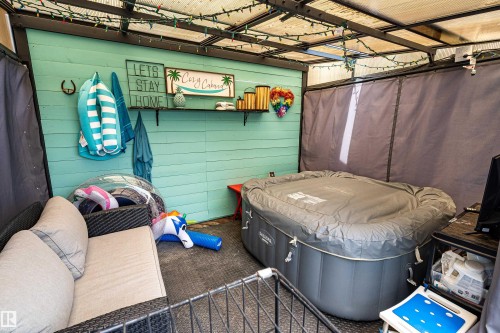 Outdoor covered patio space featuring a turquoise shiplap accent wall, built-in shelving, string lighting, and an inflatable hot tub - 21384 88 Avenue, Edmonton, AB 