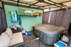 Outdoor covered patio space featuring a turquoise shiplap accent wall, built-in shelving, string lighting, and an inflatable hot tub - 