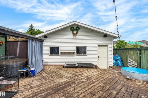 Expansive outdoor deck featuring wood-finish flooring, white vinyl siding, a dedicated side door, and a covered structure with draping - 21384 88 Avenue, Edmonton, AB 