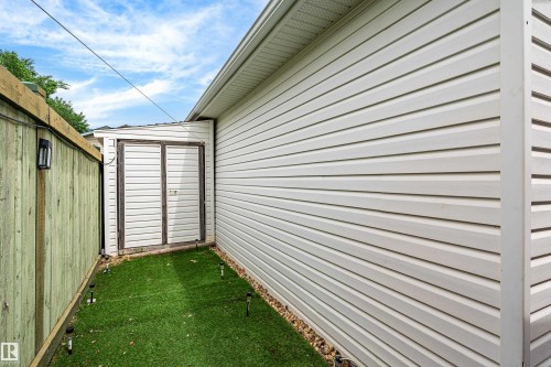 Exterior storage shed with double doors, white vinyl siding, and green fencing - 21384 88 Avenue, Edmonton, AB 