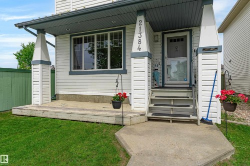 Front exterior featuring white siding with dark trim, a covered porch with decorative pillars, a concrete walkway, and a manicured lawn - 21384 88 Avenue, Edmonton, AB 