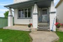 Front exterior featuring white siding with dark trim, a covered porch with decorative pillars, a concrete walkway, and a manicured lawn - 21384 88 Avenue, Edmonton, AB 