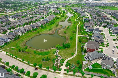 Aerial view of a residential neighborhood featuring homes with varied architectural styles, a prominent parkway with walking paths, and multiple ponds with a fountain feature - 21384 88 Avenue, Edmonton, AB 