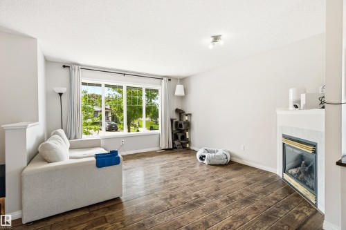 Spacious living area featuring wide-plank wood-finish flooring, a prominent bay window, and a built-in fireplace with a stone surround - 21384 88 Avenue, Edmonton, AB 