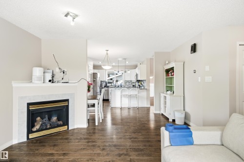 Open-concept living space featuring wood-finish flooring, a corner fireplace with a light-colored tile surround and white mantel, and ceiling-mounted track lighting - 21384 88 Avenue, Edmonton, AB 