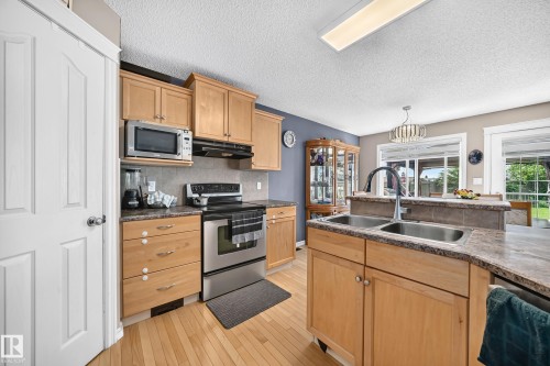 Kitchen featuring wood-finish cabinetry, stainless steel appliances, a double basin sink with a high-arc faucet, and granite-look countertops - 3224 26 Street, Edmonton, AB 