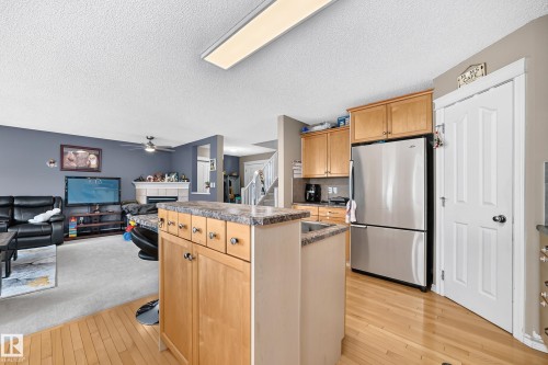Kitchen featuring wood-finish flooring, light wood cabinetry, stainless steel refrigerator, and a kitchen island with a stone-finish countertop - 3224 26 Street, Edmonton, AB 