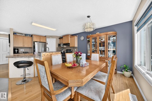 Open-concept dining area featuring wood-finish flooring, a contemporary chandelier, and a built-in display cabinet - 3224 26 Street, Edmonton, AB 
