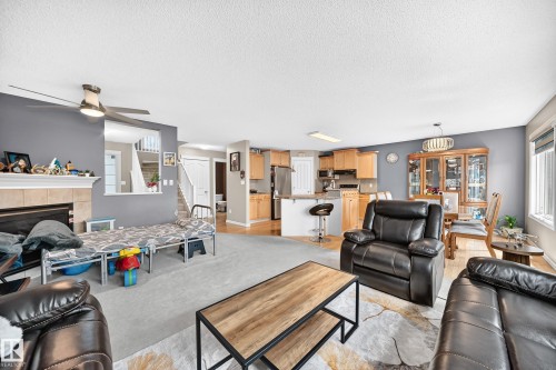 Spacious living area featuring a fireplace with a mantel, a ceiling fan, and carpeted flooring - 3224 26 Street, Edmonton, AB 