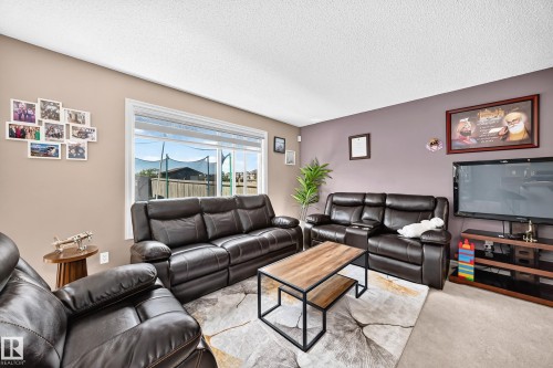 Living area featuring a large window with white trim, light beige and plum-colored walls, and textured ceiling - 3224 26 Street, Edmonton, AB 
