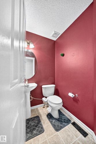 Compact powder room featuring a pedestal sink, round mirror, and tile flooring - 3224 26 Street, Edmonton, AB 