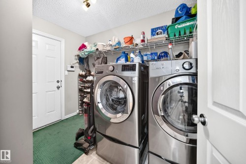 Dedicated laundry area featuring front-loading appliances, overhead wire shelving for storage, and a paneled white door - 3224 26 Street, Edmonton, AB 