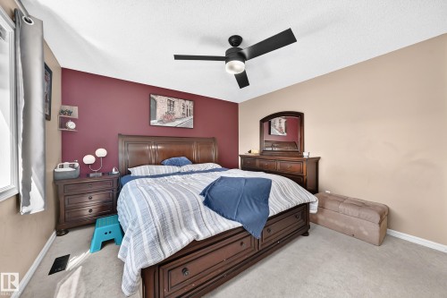 Spacious room featuring a dark wood bed frame with integrated storage drawers, a coordinating dresser and mirror, and a contemporary ceiling fan - 3224 26 Street, Edmonton, AB 