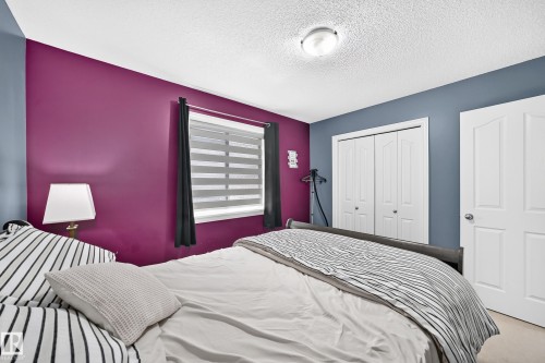 Bedroom featuring a window with blinds, bi-fold closet doors, a paneled door, and a ceiling-mounted light fixture - 3224 26 Street, Edmonton, AB 