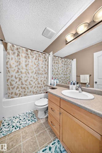 Full bathroom featuring a single vanity with wood-finish cabinetry, a neutral countertop, and an integrated sink with a chrome faucet - 3224 26 Street, Edmonton, AB 