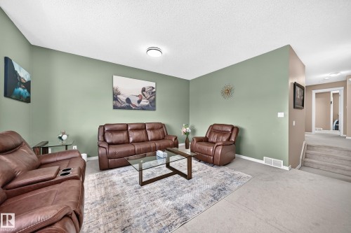 Spacious living area featuring light green walls, a flat white ceiling, and gray carpet flooring - 3224 26 Street, Edmonton, AB 