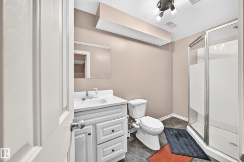 Bathroom featuring a white vanity with a single basin sink, a wall-mounted mirror, and a glass-enclosed shower with a frosted panel - 3224 26 Street, Edmonton, AB 