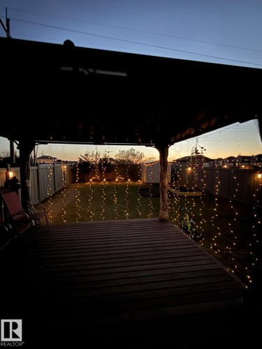 Covered deck featuring wood plank flooring, string lighting, and a fenced backyard - 3224 26 Street, Edmonton, AB 