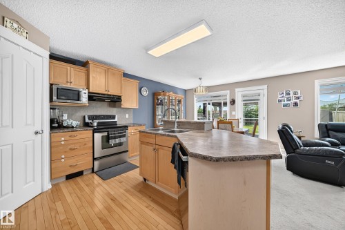Kitchen featuring wood-finish flooring, light wood cabinetry, stainless steel appliances, and an island with an integrated sink - 3224 26 Street, Edmonton, AB 