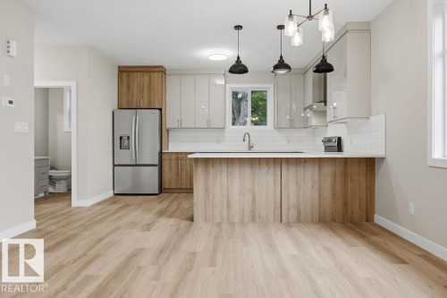 Modern kitchen featuring wood-finish flooring, two-tone cabinetry, stainless steel appliances, white subway tile backsplash, and a contemporary island with pendant lighting - 6204 150 Avenue, Edmonton, AB 