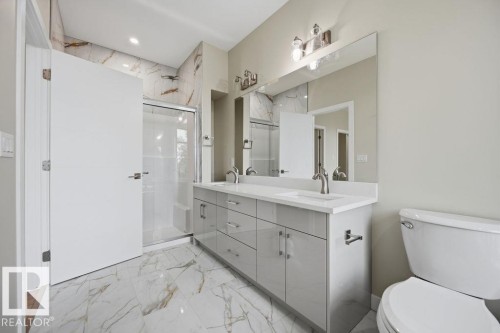 Double vanity with light gray cabinetry and white countertops, complemented by a large frameless mirror and modern brushed nickel fixtures - 6204 150 Avenue, Edmonton, AB 
