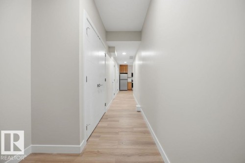 Hallway featuring wood-finish flooring, white baseboards, multiple panel doors with brushed nickel hardware, recessed lighting, and neutral wall tones - 6204 150 Avenue, Edmonton, AB 