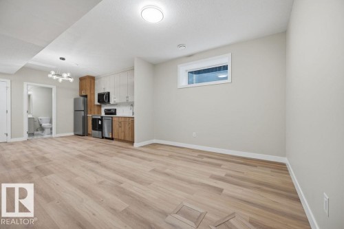Open-concept living area featuring wood-finish flooring, a contemporary chandelier, a compact kitchen with stainless steel appliances, and a recessed window - 6204 150 Avenue, Edmonton, AB 