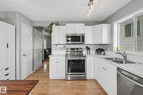 Modern kitchen featuring white cabinetry, stainless steel appliances, marble-look countertops, and wood-finish flooring - 2123 36 Avenue, Edmonton, AB - Indoor Photo Showing Kitchen With Double Sink