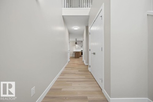 Hallway featuring wood-finish flooring, light grey painted walls, white trim, and a contemporary ceiling light fixture - 15004 62 Street, Edmonton, AB 