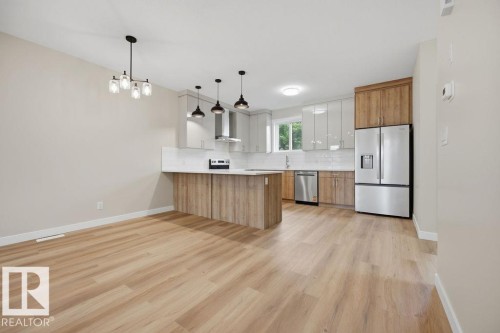Open-concept kitchen and dining area featuring wood-finish flooring, two-tone cabinetry, stainless steel appliances, a white tile backsplash, and a contemporary pendant chandelier - 15004 62 Street, Edmonton, AB 