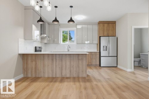 Modern kitchen featuring a two-toned island, light wood-finish flooring, and a stainless steel refrigerator - 15004 62 Street, Edmonton, AB 