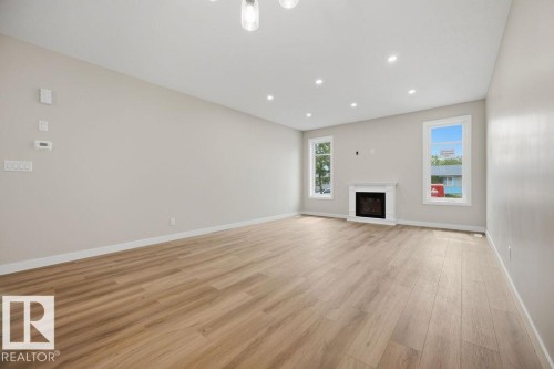 Spacious interior living area featuring wood-finish flooring, a white mantel fireplace, and recessed lighting - 15004 62 Street, Edmonton, AB 